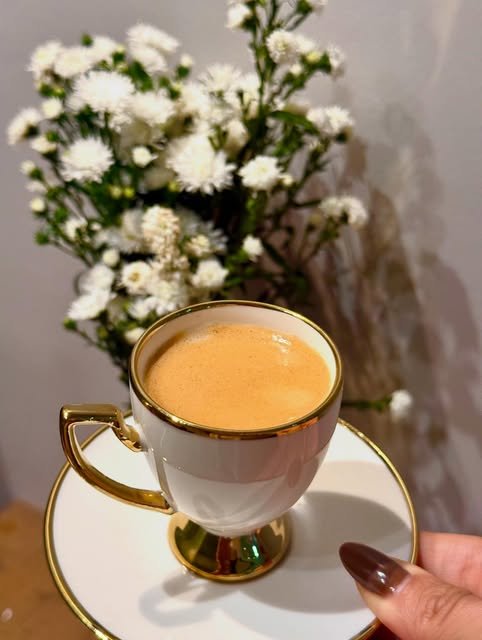 Xícara de café com borda dourada e flores brancas no espaço da Simone